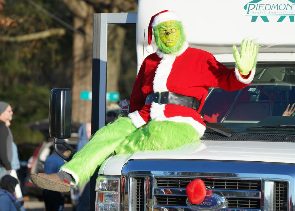 Eine als Grinch verkleidete Person sitzt auf der Motorhaube eines Trucks.