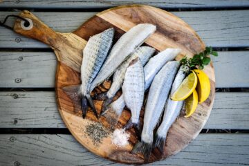 Sieben Fische (ohne Köpfe) auf einem Holzbrett, serviert mit Zitrone